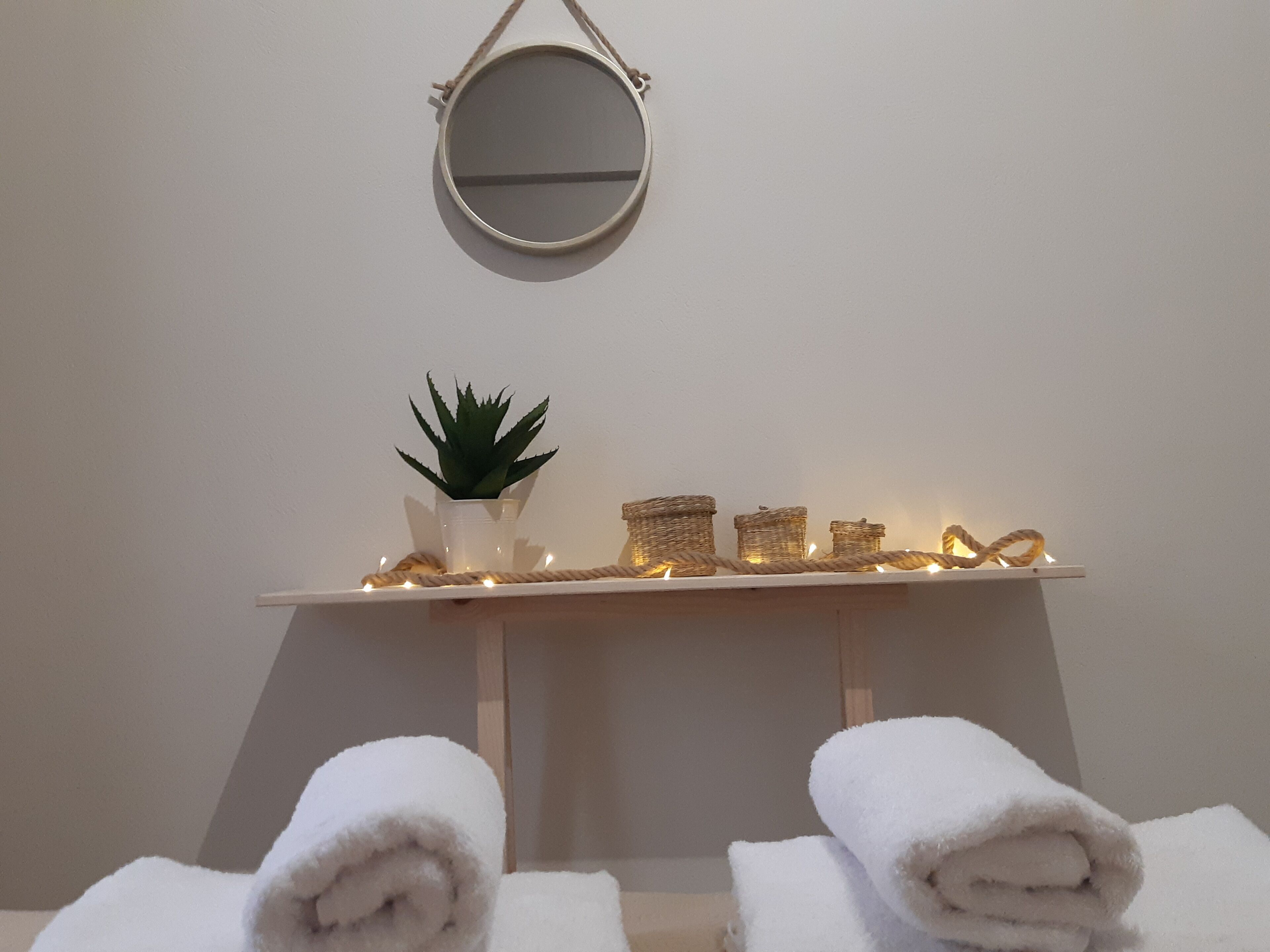 A bathroom with a mirror, a small potted plant, and a shelf with decorative jars and lights.