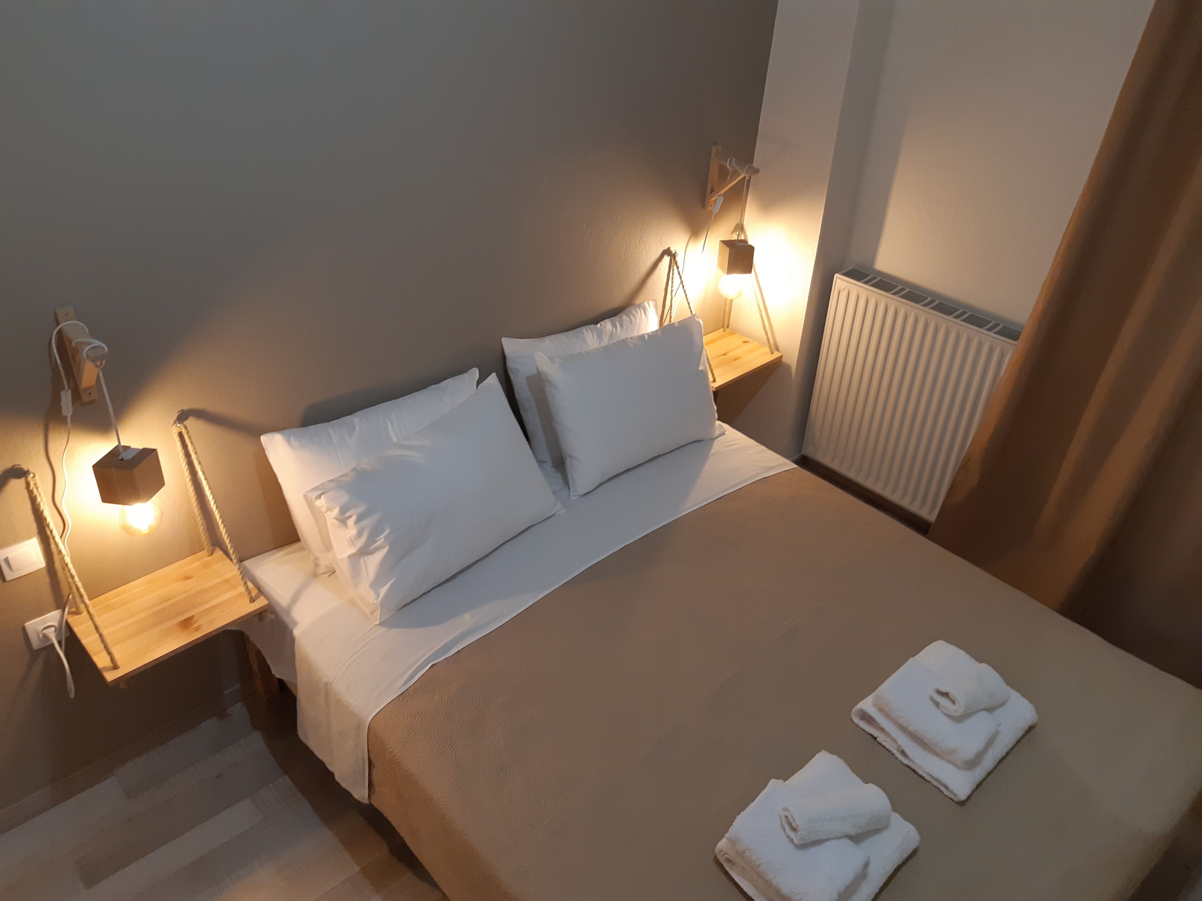 Ein ordentlich bezogenes Bett mit weißen Leinentüchern, zwei Nachttischlampen und einem Heizkörper in der Ecke.