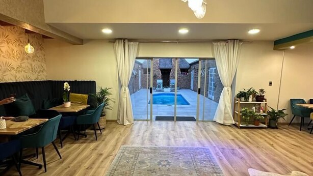Une pièce spacieuse avec un plafond en bois, une grande moquette, un coin repas avec des chaises et une table, et une vue sur une piscine à travers des portes vitrées.