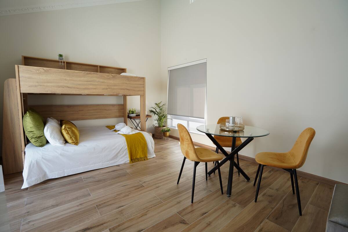 A room with a bunk bed, a dining table with chairs, and a large window.