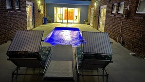 Un jardin avec une piscine, deux chaises longues et une table de patio.