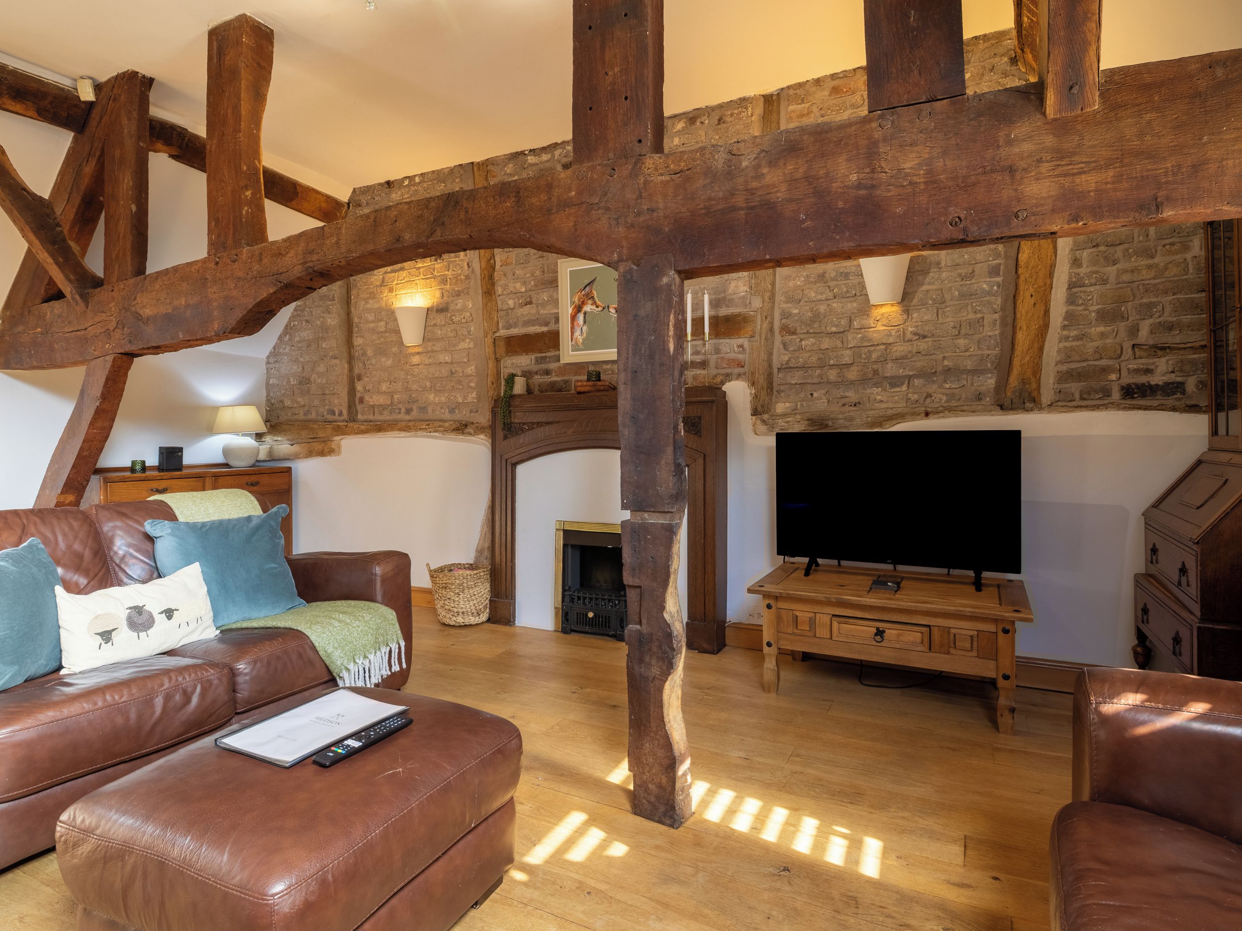 A rustic living room with exposed wooden beams, a fireplace, a television, and leather furniture.