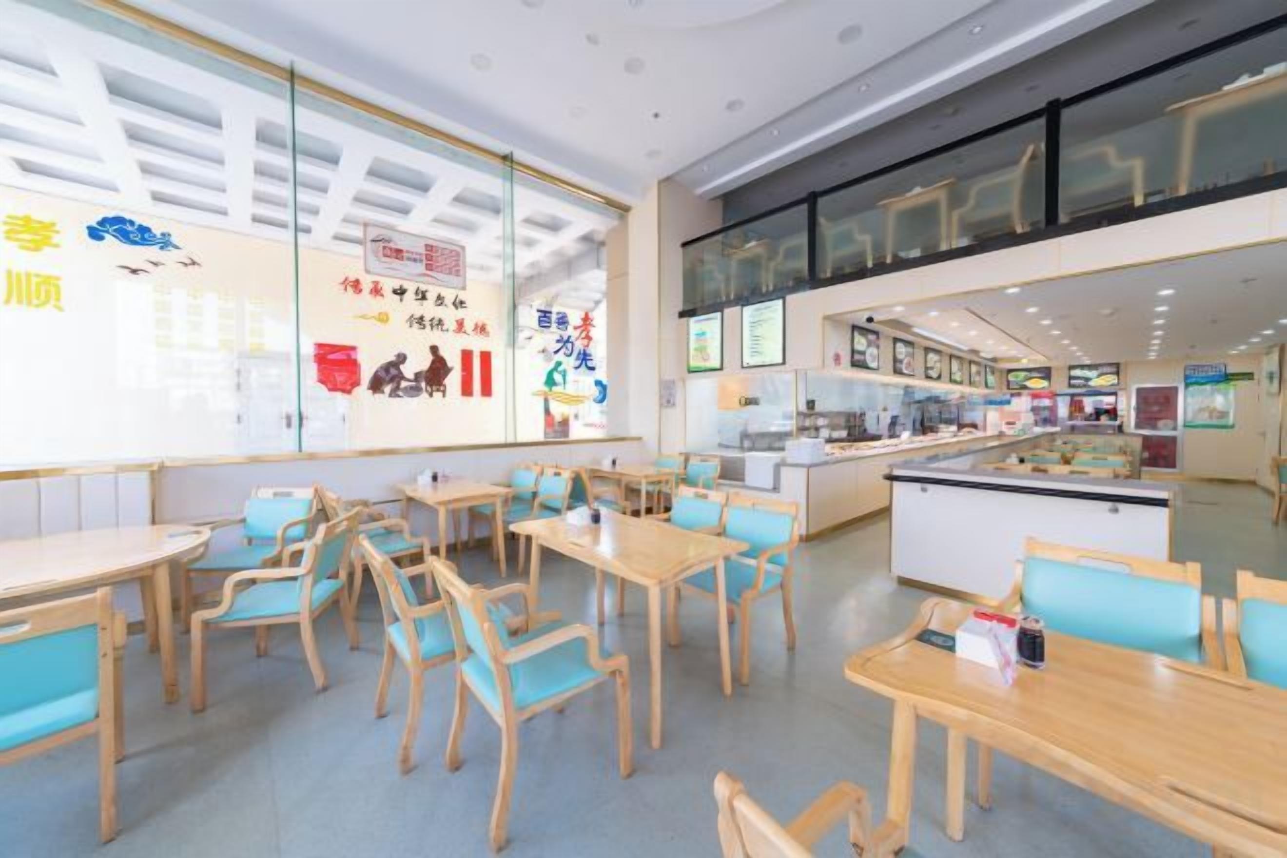 A restaurant with multiple tables and chairs, a counter with a display case, and a wall with various signs and posters.