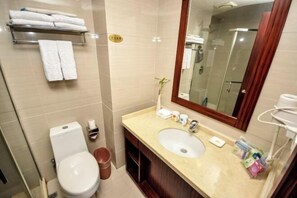 A bathroom with a toilet, sink, and mirror. There are towels on a shelf and a trash bin. - Xinhui Hotel (Zhoushan)