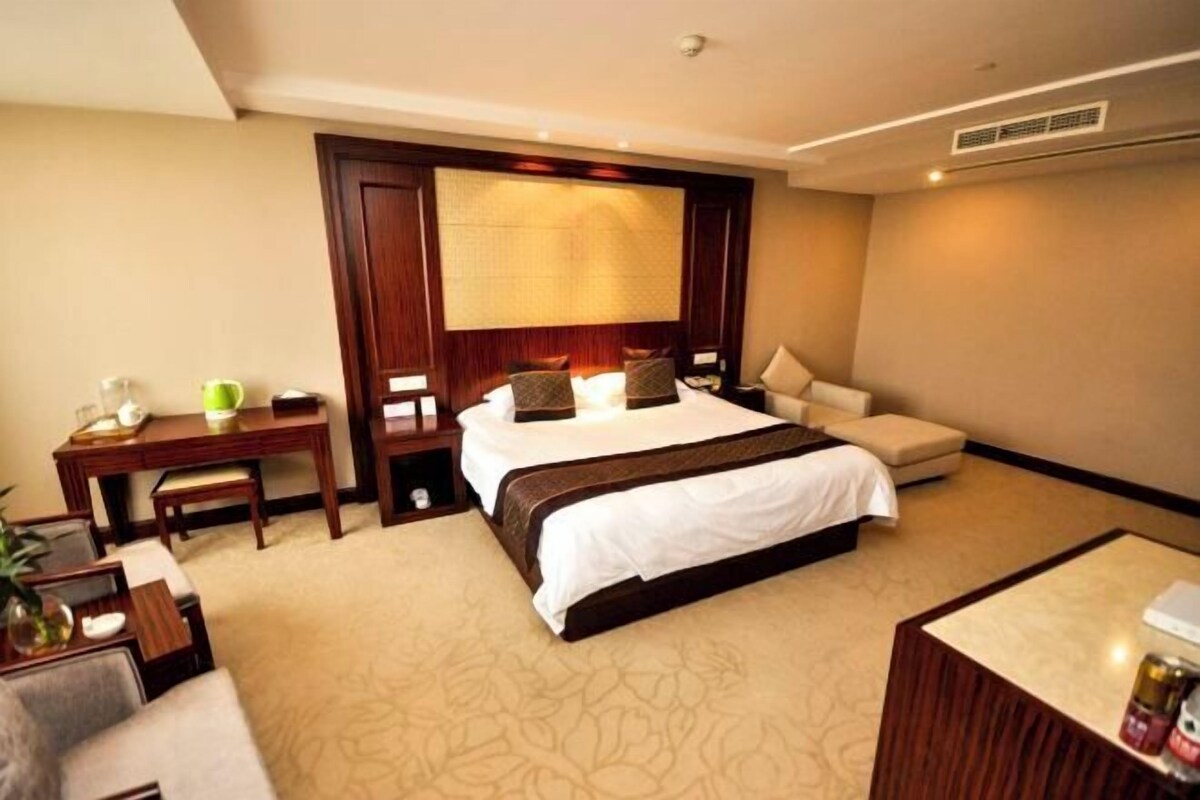 A hotel room with a large bed, a desk, a chair, a sofa, and a small table.