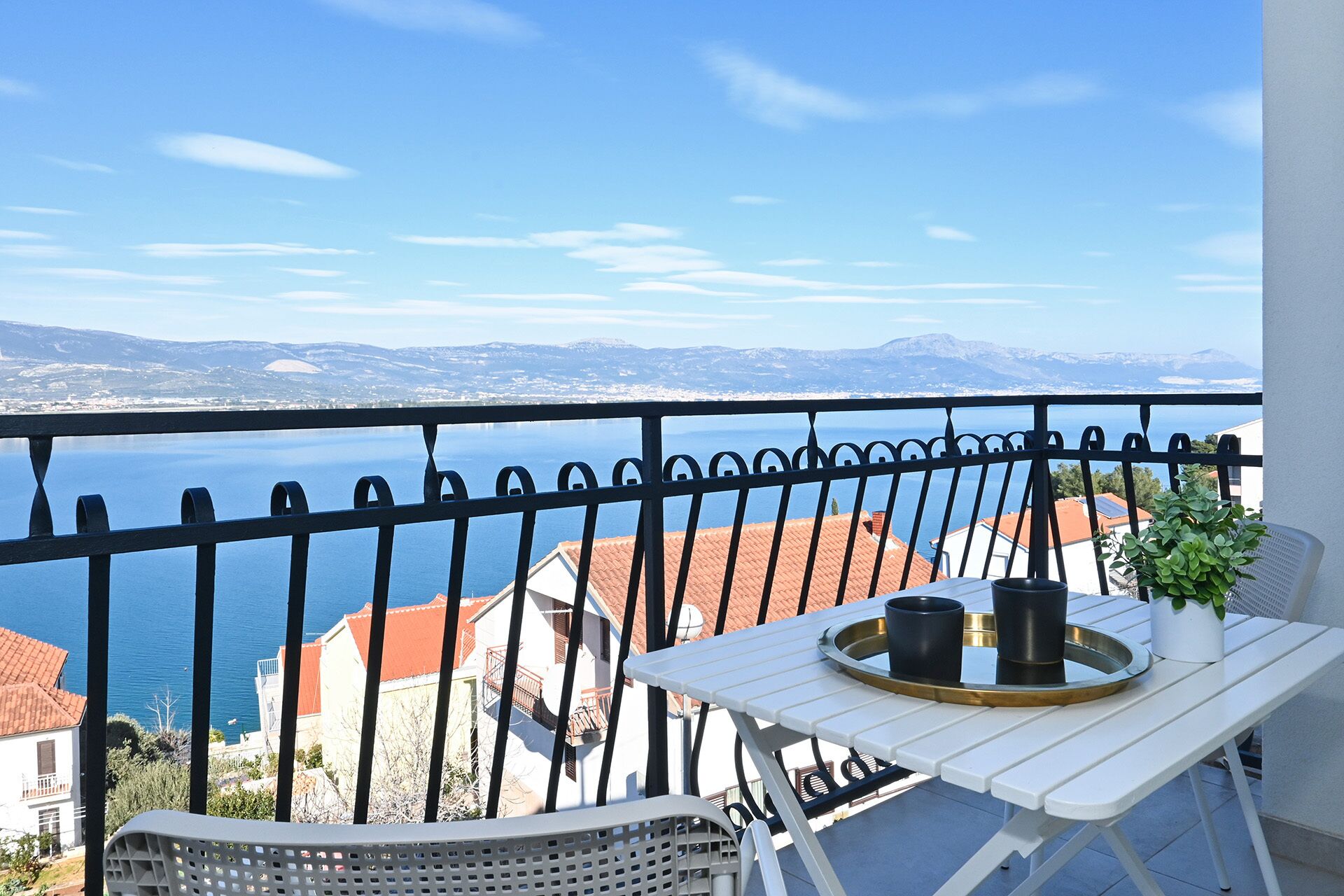 A balcony with a table and chairs, overlooking a body of water and distant mountains.