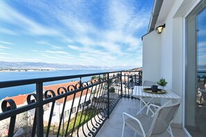 A balcony with a table and chairs, overlooking a body of water and a cityscape.