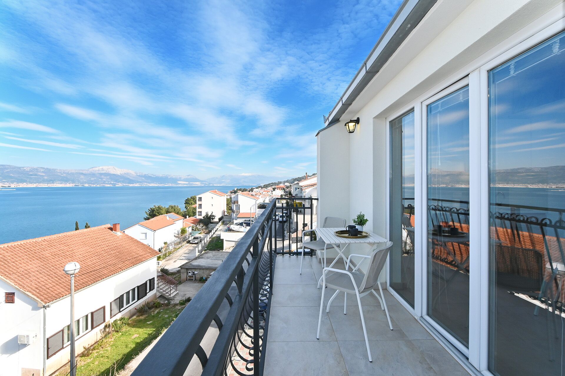 Un balcon avec une table et des chaises, donnant sur une étendue d’eau et une ville côtière.