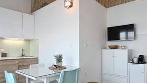 A modern kitchen with white cabinetry, a glass dining table, teal chairs, a small potted plant, and a TV mounted on the wall. - Grigic 4, modern 1 bedroom apartment (Mastinka)