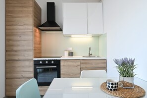 A modern kitchen with a stove, oven, and white cabinetry. There is a dining table with chairs and a coffee mug.