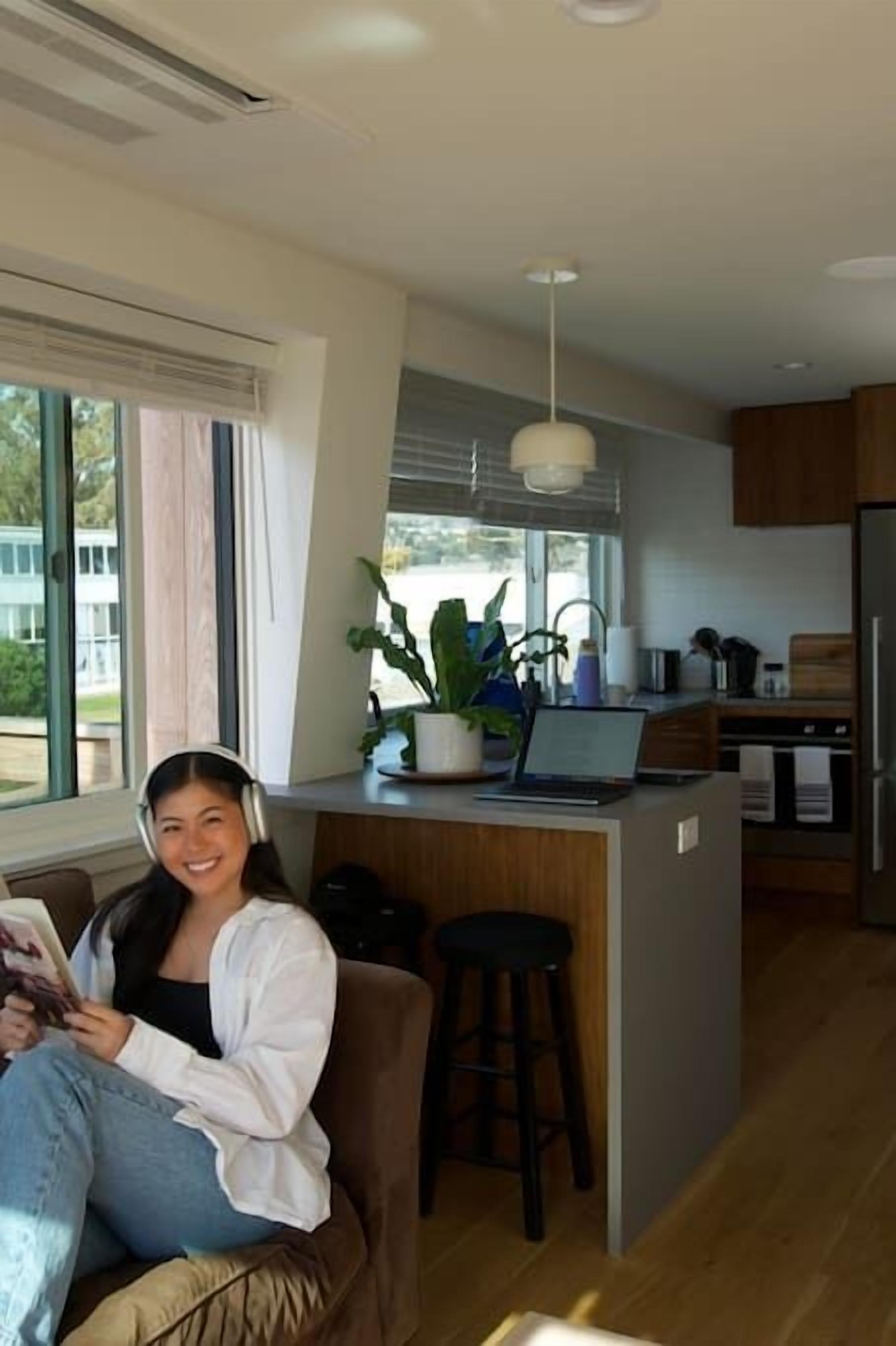 A modern kitchen with a central island, a dining area with a bar stool, and a large window providing a view of the outdoors.