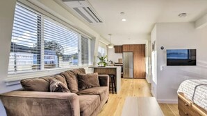 Un espai habitable compacte amb un sofà, una taula petita, un llit, una zona de cuina i un televisor fixat a la paret.