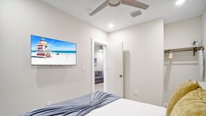 A bedroom with a bed, a ceiling fan, a painting of a beach scene, and a door leading to another room. - Stylish East Little Havana Flats (Miami)
