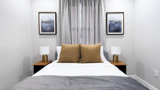 A neatly arranged bedroom with a bed, two bedside lamps, and two framed artworks on the wall. - Stylish East Little Havana Flats (Miami)