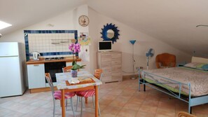 Ein kleines Zimmer mit Küchenzeile, Esstisch mit Stühlen, einem Bett und einem kleinen Kleiderschrank.