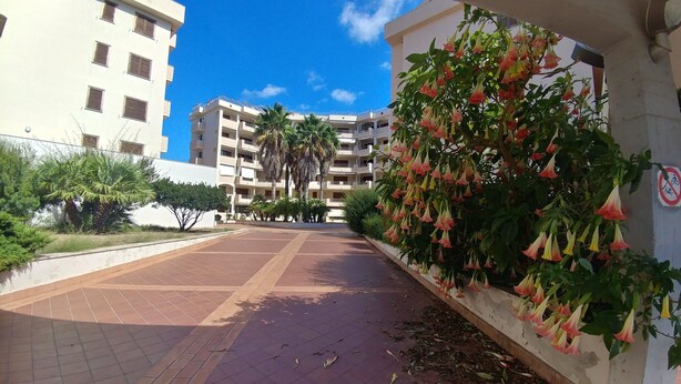 A residential building with multiple balconies, a paved walkway, and a wall with hanging flowers. - Hi Studio with beautiful sea view 🌅 Air Conditioning  (Alghero)