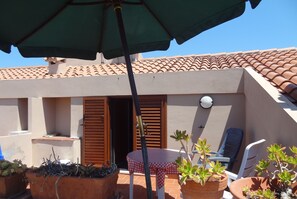 Um terraço com vasos de terracota, uma mesa com toalha xadrez e uma cadeira.