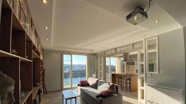 Un salón amplio con un sofá gris, una mesita y una estantería. Una ventana grande ofrece vistas de la ciudad.