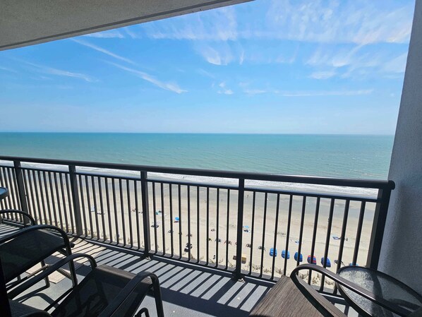 A balcony with a view of the beach, metal chairs, and a railing.