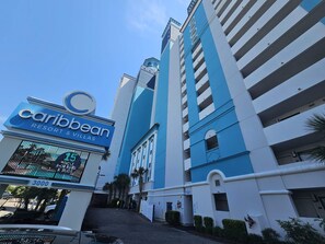 Um edifício alto com esquema de cores azul e branco, uma placa com a inscrição 'Caribbean Resort & Villas' e uma entrada visível com o número '3000' na porta.
