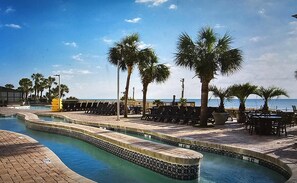 A pool area with lounge chairs and palm trees, overlooking a beach.