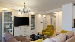 A modern living room with a flat-screen TV, a chandelier, a sofa set, and a glass cabinet. - Apartment with Balcony No.18 in Nar Residence (Porec)