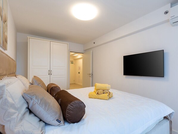 A hotel room with a bed, pillows, a TV, and an exit door. - Apartment with Balcony No.18 in Nar Residence (Porec)