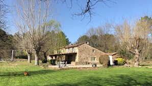 Ein Steinhaus mit Terrasse, umgeben von Bäumen und einem gepflegten Rasen.