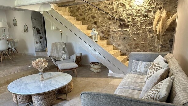 Ein Wohnzimmer mit Steinwand, einer Treppe, einem runden Tisch und einem grauen Sofa.