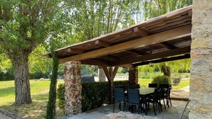 Ein Außenbereich mit einer Terrasse, Steinpfeilern, einer Holzpergola und einem Tisch mit Stühlen.