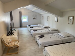 Une chambre avec quatre lits simples, un bureau avec une chaise, un ours en peluche et une fenêtre avec des rideaux.