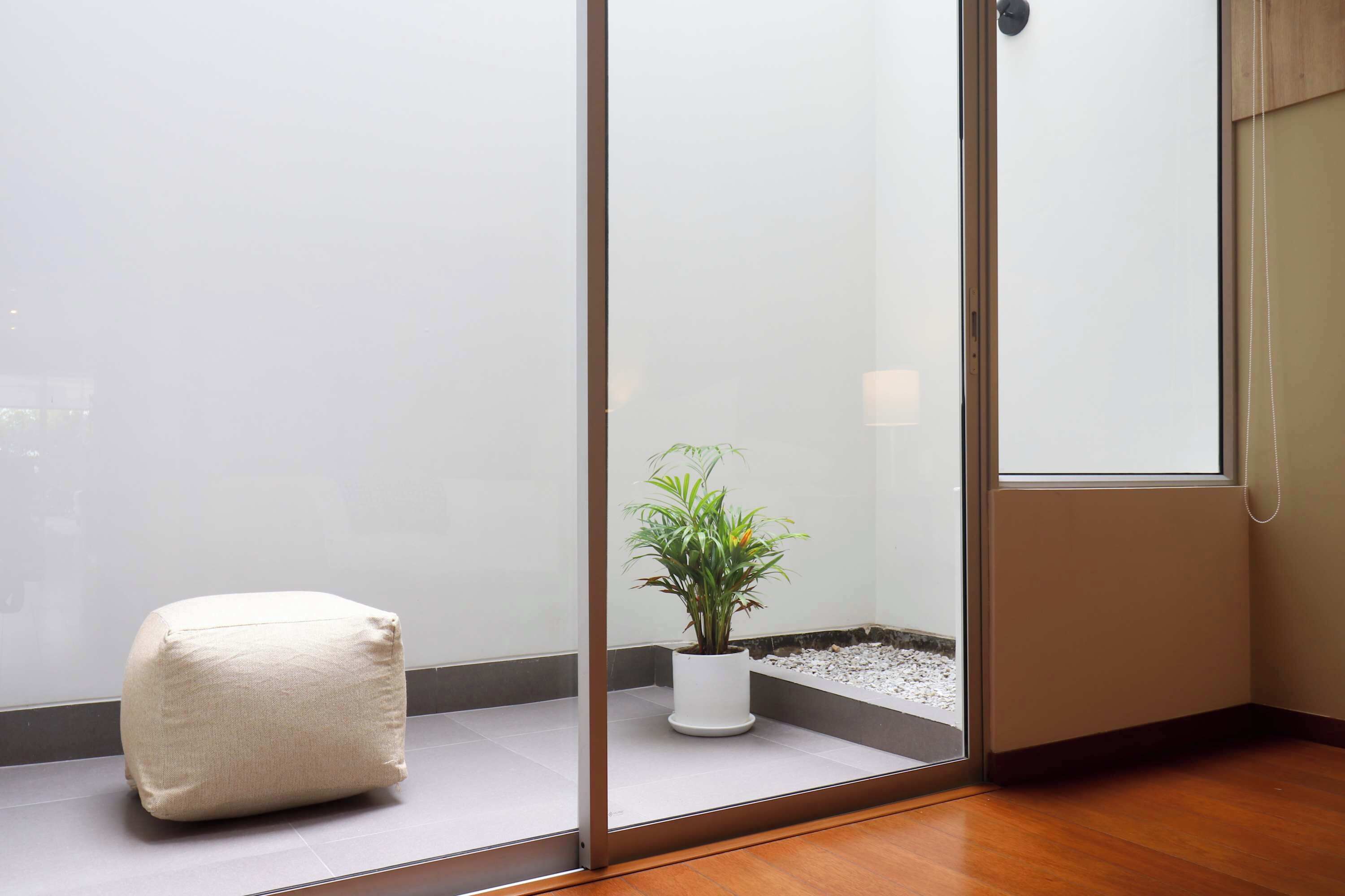 Un coin de pièce avec une cloison en verre, une plante en pot et un coussin blanc.