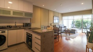 A modern kitchen with built-in appliances, a dining area with a sofa and chairs, and large windows offering a view of the outdoors. - w* | Spectacular 1BR w/ Terrace in Miraflores (Lima)