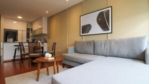 A modern living room with a grey sofa, a wooden coffee table, and a dining area with chairs and a kitchen in the background. - w* | Spectacular 1BR w/ Terrace in Miraflores (Lima)