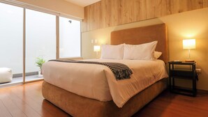 A modern hotel room with a large bed, wooden panel wall, sliding glass door, and bedside table with a lamp. - w* | Spectacular 1BR w/ Terrace in Miraflores (Lima)