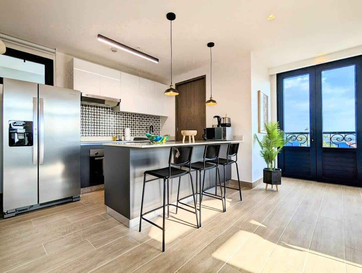 Una cocina moderna con una isla central, electrodomésticos de acero inoxidable y taburetes negros.