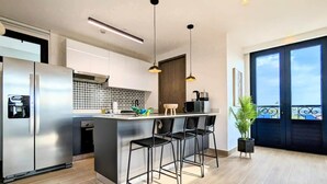 A modern kitchen with a central island, stainless steel appliances, and black bar stools.