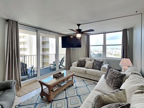 A living room with a sofa, coffee table, and a TV. There is a balcony with a view of the city.