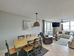 A modern living room with a dining area, a sofa, a TV, and large windows.