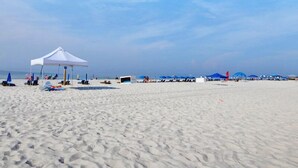 Una spiaggia con una tenda bianca, lettini e ombrelloni.