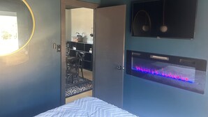 Um quarto com cama, espelho, televisão e lareira.