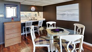 A dining area with a glass table, white chairs, and a wooden dresser. - Edgewater Windward #204 | Gulf Front + Amenities (Panama City Beach)