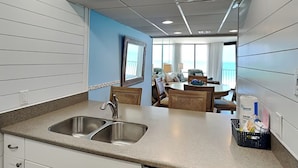 Una cocina moderna con un lavamanos doble, un comedor con mesa y sillas, y vista al océano a través de amplios ventanales.