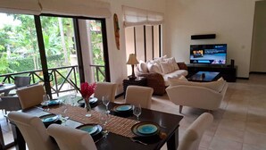 A dining area with a table set for four, a sofa, and a television in the background.