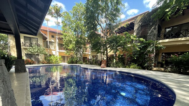 A swimming pool surrounded by lush greenery and a multi-story building with balconies.
