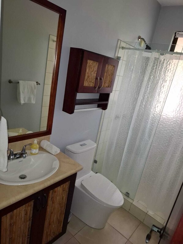 A bathroom with a sink, mirror, cabinet, toilet, and shower curtain. - 3 BR Condo Centrally Located in Playas del Coco (Playas del Coco)