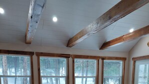 A dining area with a wooden table and chairs, large windows with a view of a snowy forest, and exposed wooden beams on the ceiling. - White Tail Cabin located on 100 private forested acres, in a Crown Game Preserve (Apsley)