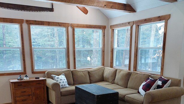 A cozy living room with a sectional sofa, a wooden chest of drawers, and large windows offering a view of trees. - White Tail Cabin located on 100 private forested acres, in a Crown Game Preserve (Apsley)