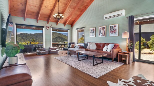 A spacious living area with a wooden ceiling, a large sofa set, a coffee table, and a view of the outdoors. - Alpine Twin Heights (Merrijig)