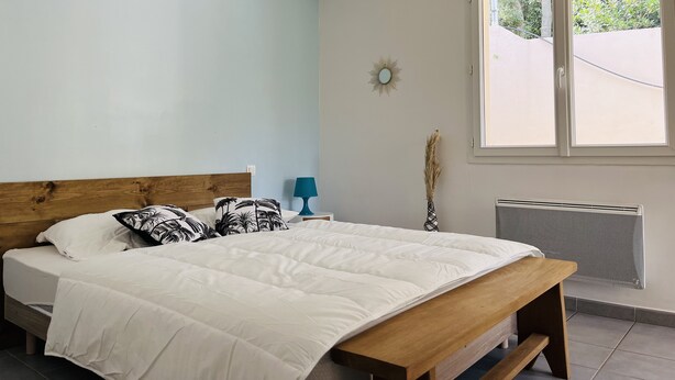 Une chambre à coucher comprenant un lit, un banc en bois, une fenêtre, un radiateur et un luminaire fixé au mur.